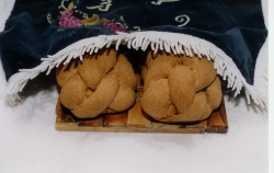 Two braided Shabbat challahs placed under an embroidered challah cover at the start of the Shabbat meal